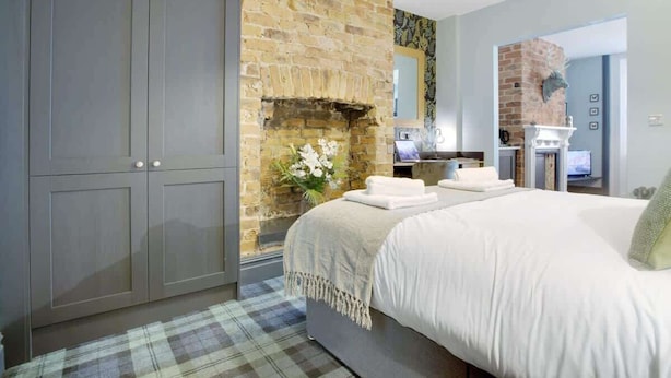 A bedroom with a large bed, a brick fireplace, a wardrobe, and a television in the corner. - 15a Furness House (Hartlepool)
