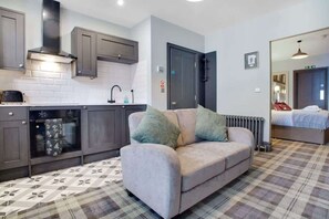 A compact living space with a kitchenette, a sofa with cushions, a patterned floor, and a bed in the background.
