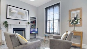 A living room with a fireplace, two armchairs, a coffee table, and a bookshelf.