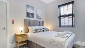 A bedroom with a bed, bedside tables, a window with blinds, and wall art.