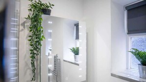 A bathroom with a large mirror, a potted plant, and a window with a view.
