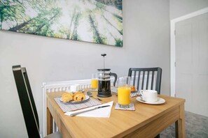 A breakfast table with croissants, a coffee maker, and orange juice glasses.