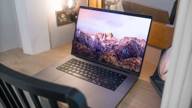 A laptop on a wooden table with a mountain wallpaper, a chair, and a lamp with a globe.