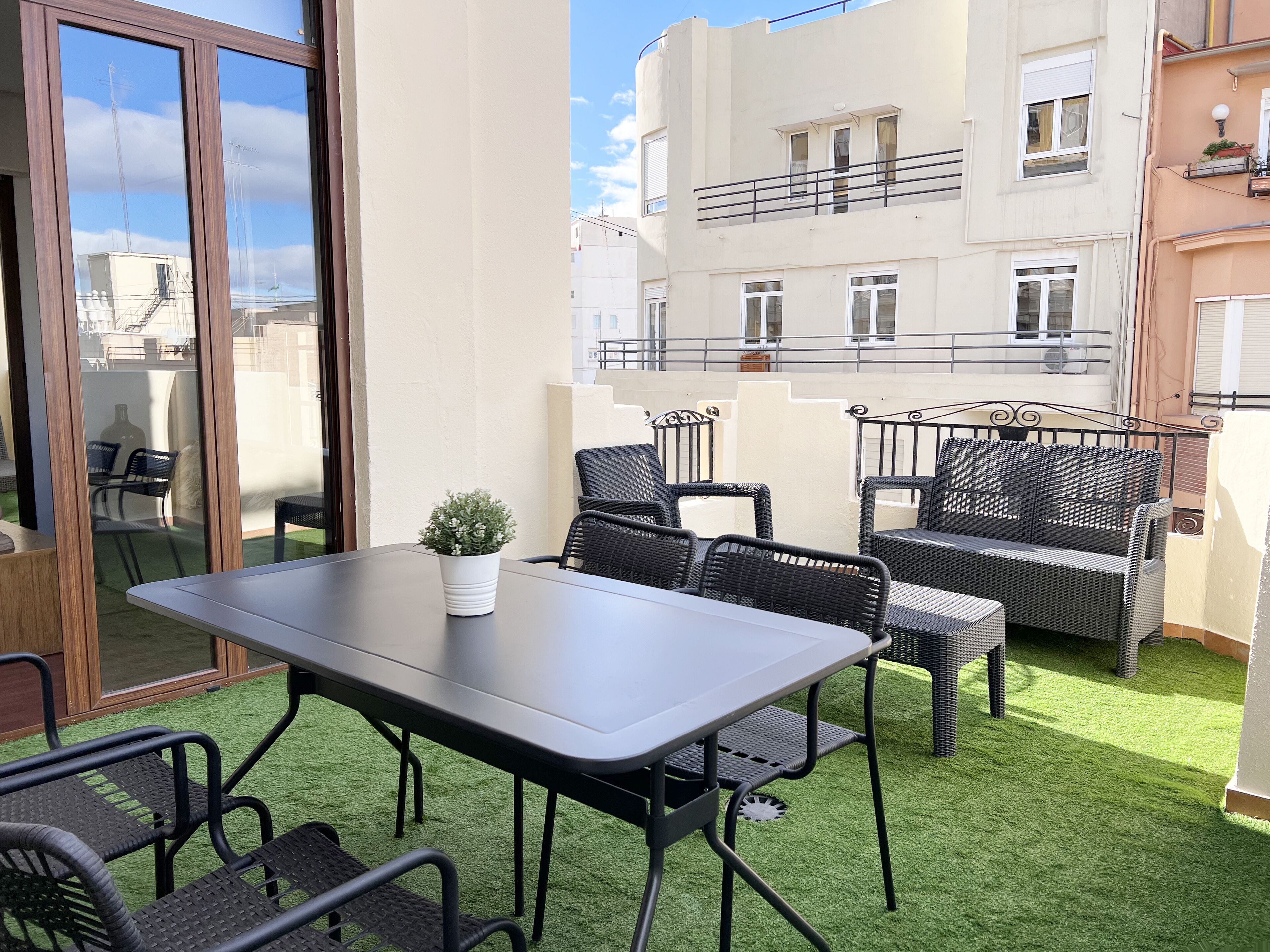 A balcony with a table and chairs, a small potted plant, and a view of neighboring buildings.