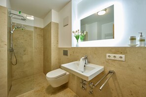 A modern bathroom with a glass shower enclosure, a white toilet, a sink with a towel, and a mirror above the sink. - The perfect retreat in the Bavarian Alps - welcome to the Mountain Lodge! (Garmisch-Partenkirchen)