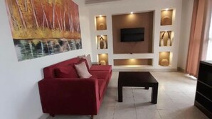 A modern living room with a red sofa, a coffee table, a flat-screen TV mounted on the wall, recessed lighting, and a large painting on the wall.