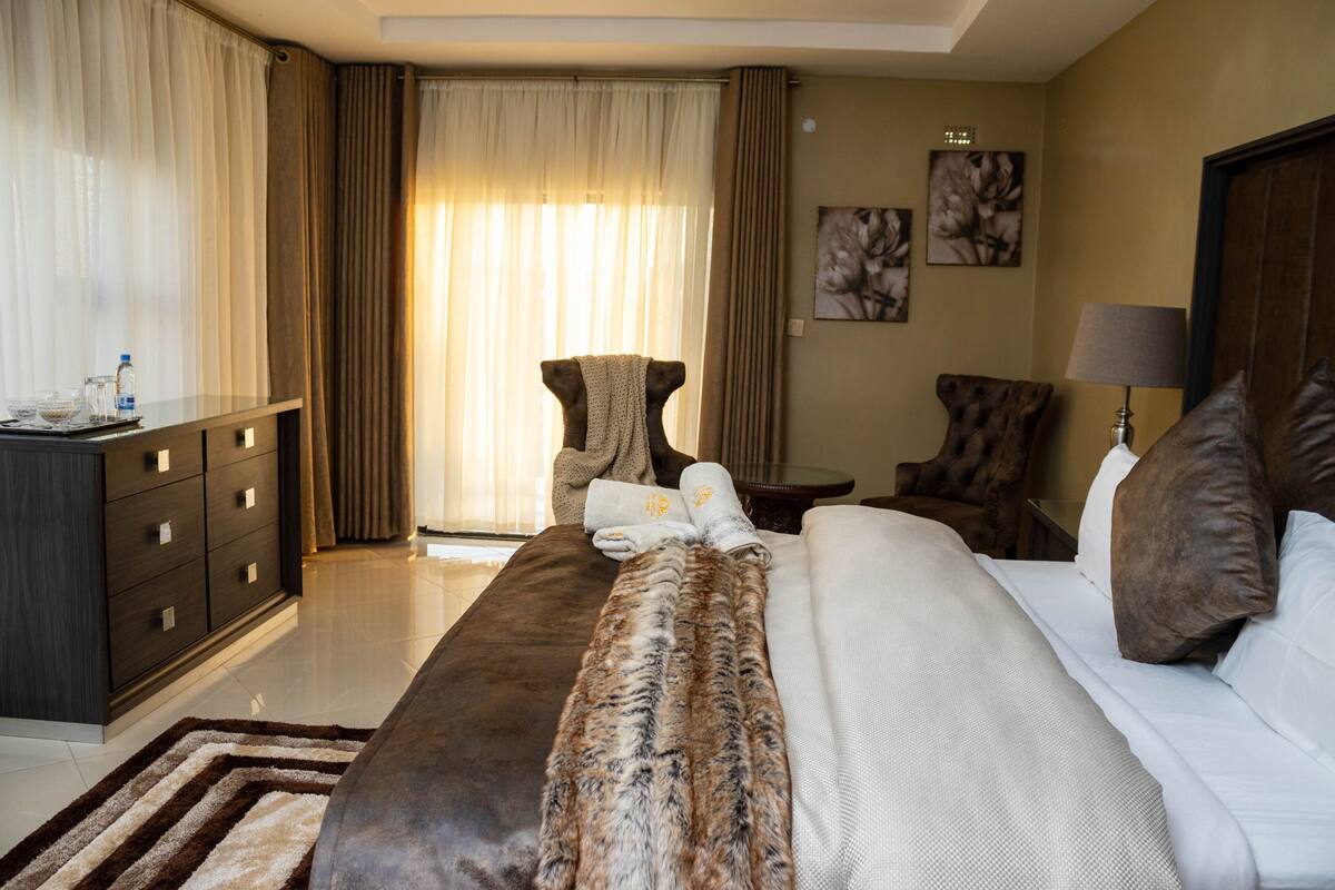 A hotel room with a bed, a desk, a chair, a lamp, and a window with curtains.