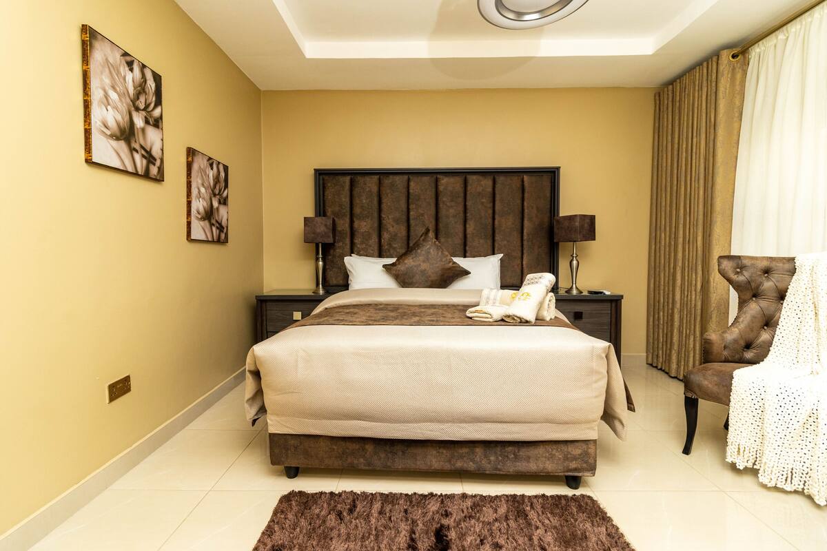 A hotel room with a large bed, a nightstand, a chair, and artwork on the walls.