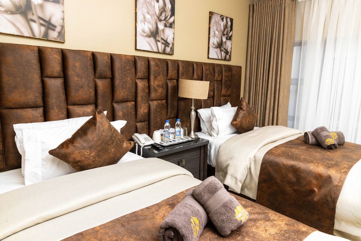 A hotel room with two beds, a nightstand with a lamp, a phone, and toiletries.