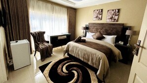 A hotel room with a bed, a chair, a desk, a lamp, and a ceiling fan. - URBAN LIFESTYLES HOTEL (Masvingo)