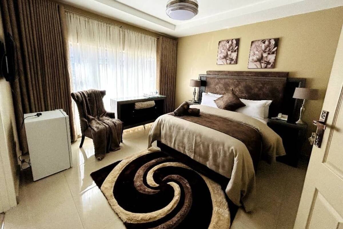 A hotel room with a bed, a chair, a desk, a lamp, and a ceiling fan.