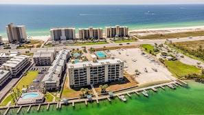 Un hotel frente al mar con varias construcciones, un puerto deportivo y una playa.