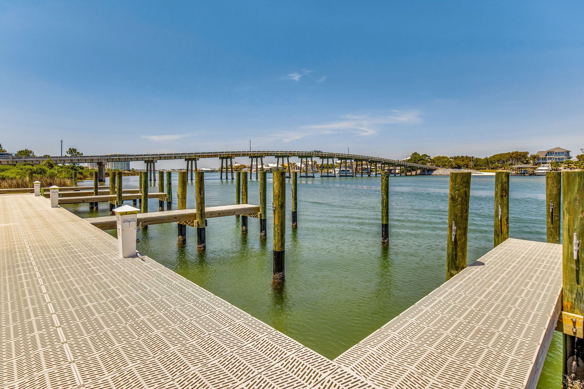 Une jetée avec une passerelle en bois s’étendant sur une étendue d’eau calme, un pont en arrière-plan et une maison avec un quai.