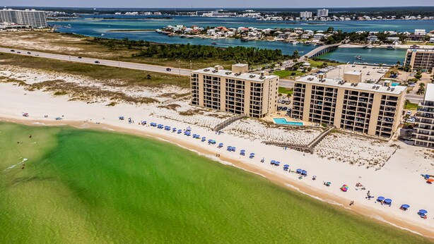 A coastal hotel with multiple high-rise buildings, a beach with umbrellas, and a clear view of the ocean. - Wind Drift Orange Beach - Bay Views - Boat Slips - 3BR Dual-Waterfront Sleeps 11 (Orange Beach)