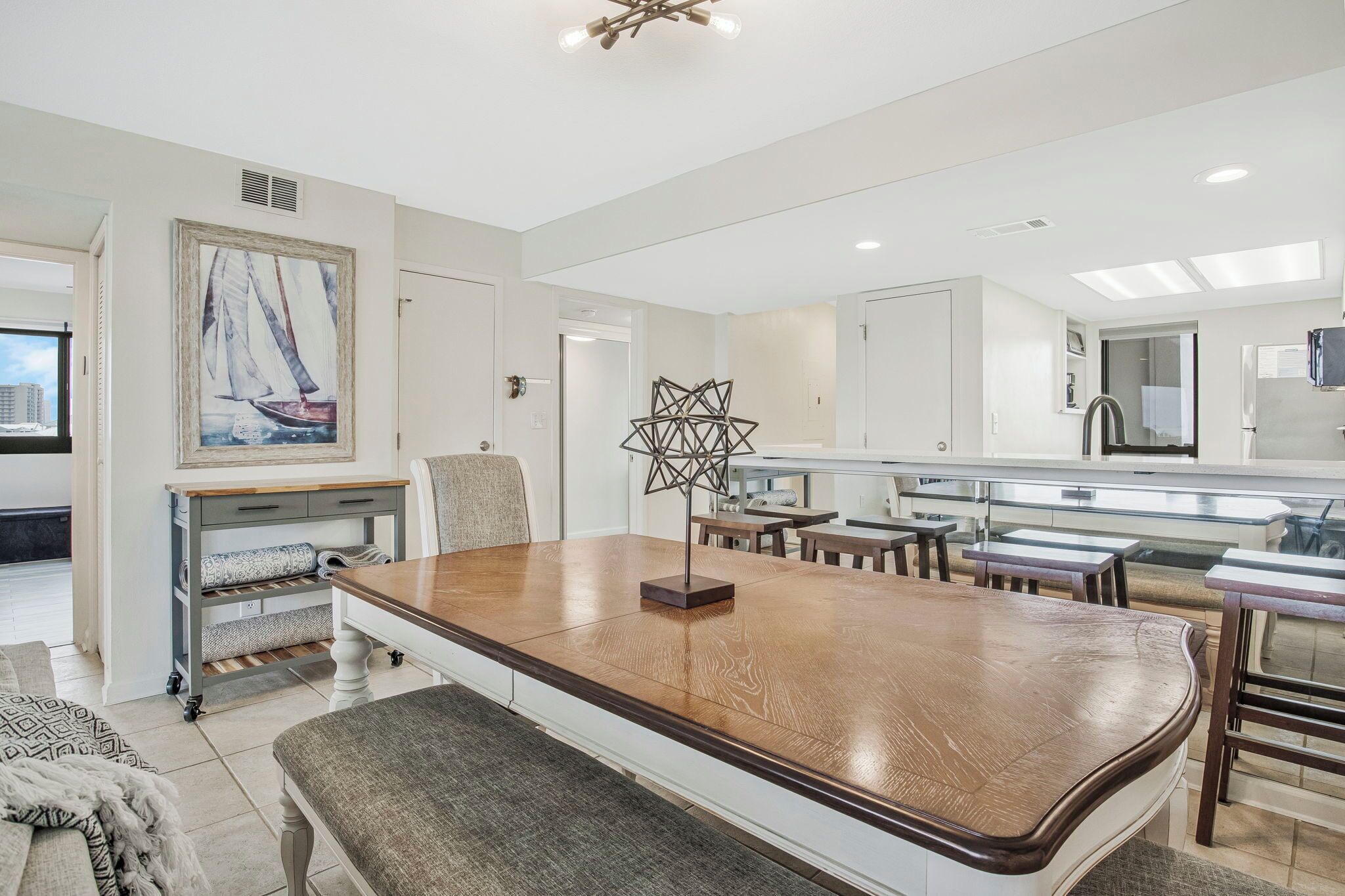 A modern kitchen with a long wooden table, a painting of a sailboat, and a geometric light fixture.