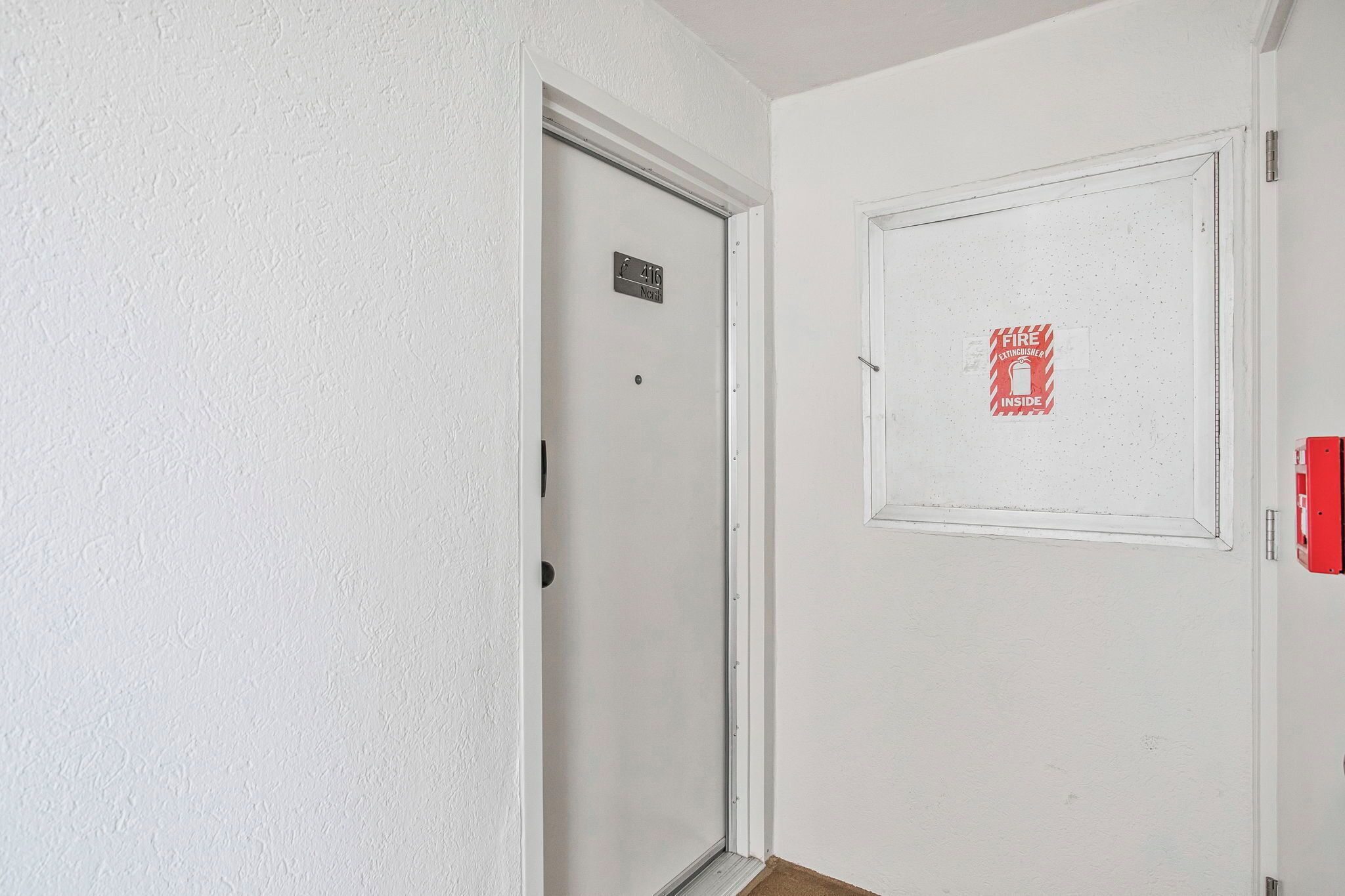A white door with a fire extinguisher sign, a door number sign, and a red emergency exit sign.