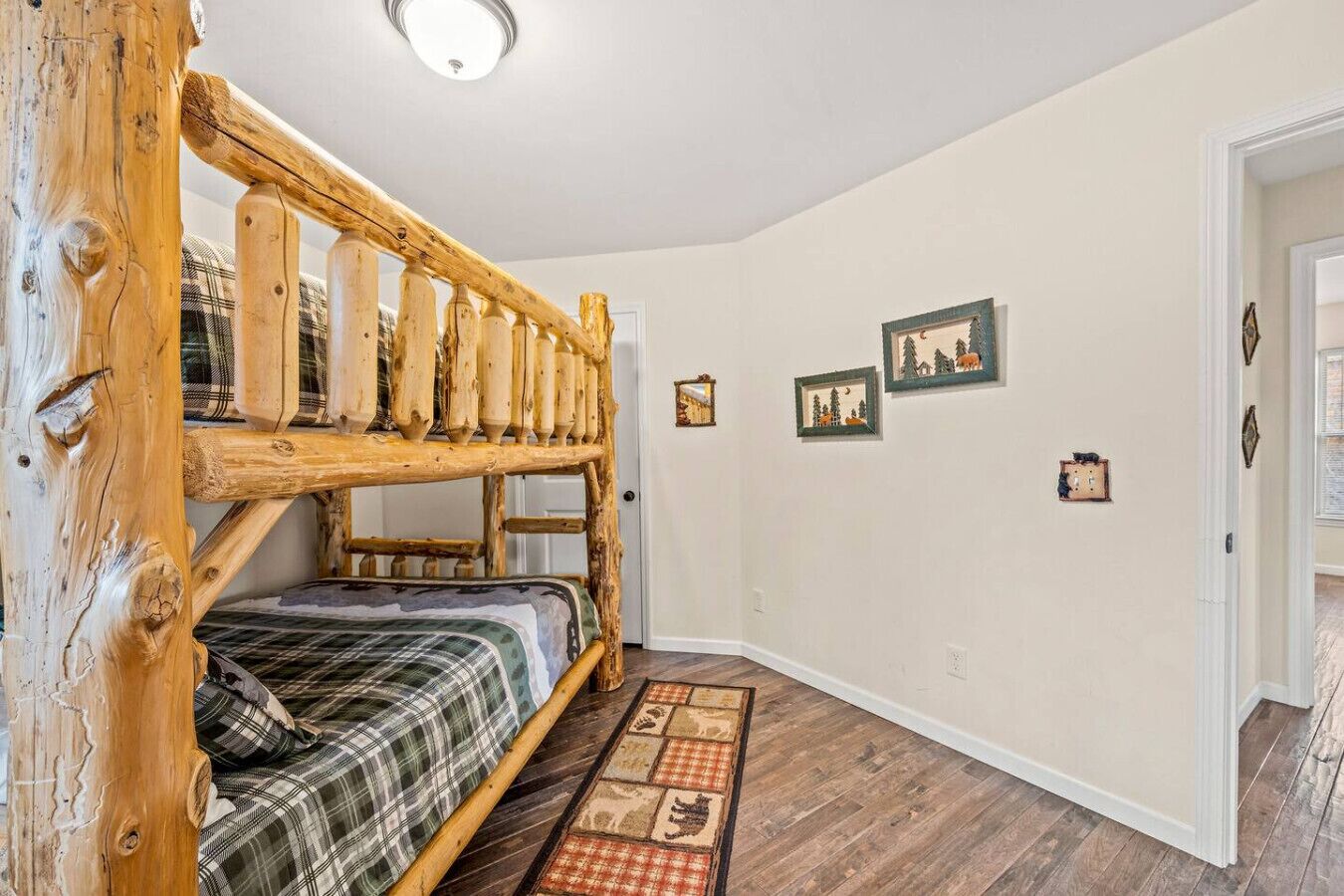 Una habitación con una cama litera, una escalera de madera, una colcha escocesa, piso de madera y tres cuadros en la pared.