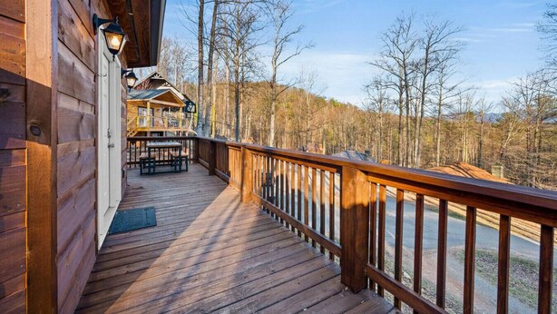 A wooden deck with a railing, a covered seating area, and a view of a forested landscape.