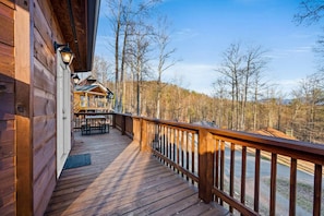 Een houten terras met een balustrade, een overdekte zithoek en uitzicht op een bebost landschap.