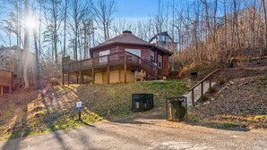 A cabin with a balcony, surrounded by trees and a gravel path leading to it.
