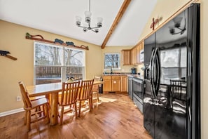 Une cuisine avec des meubles de rangement en bois, un réfrigérateur noir et une table à manger avec des chaises.