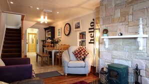 A cozy living room with a fireplace, a dining area, and a staircase leading to another level. - Ryans Roundstone Retreats Old bakery (3 bedrooms) (Roundstone)