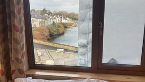 A room with a bed, a window with a view of a river and houses. - Ryans Roundstone Retreats Old bakery (3 bedrooms) (Roundstone)