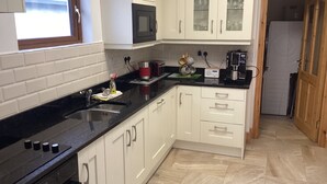A modern kitchen with white cabinets, a black countertop, a microwave, and a coffee maker. - Ryans Roundstone Retreats Old bakery (3 bedrooms) (Roundstone)