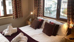 A hotel room with a bed, a bedside table, a lamp, and a view of the street outside. - Ryans Roundstone Retreats Old bakery (3 bedrooms) (Roundstone)