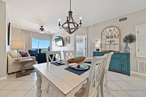 A dining area with a wooden table, white chairs, a chandelier, and a view of the outdoors.