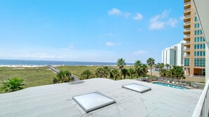 A rooftop with a pool, palm trees, and a view of the beach and ocean. - Tidewater 102- Orange Beach - 2bd/2bath - Beachfront (Orange Beach)