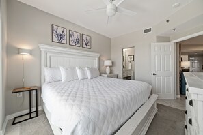 A bedroom with a white bed, a ceiling fan, and wall-mounted artwork.