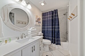 A bathroom with a white sink, a round mirror, a toilet, a bathtub, and a shower curtain.