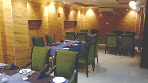 A dining area with green upholstered chairs, a blue tablecloth, and a wooden wall with a marble-like pattern. - The Royal Suite (Bhubaneshwar)