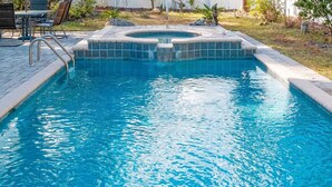 Una piscina rectangular con un jacuzzi en el centro, rodeada por una solana de baldosas y un pequeño patio con sillas.