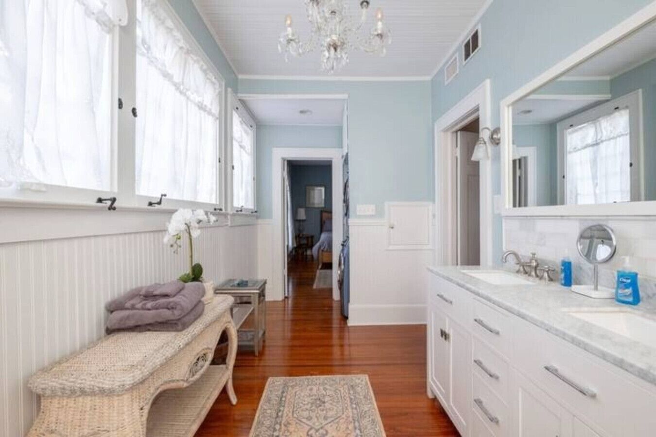 A spacious bathroom with a large mirror, white cabinetry, and a wooden floor.