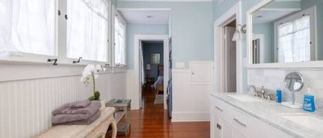 A spacious bathroom with a large mirror, white cabinetry, and a wooden floor.