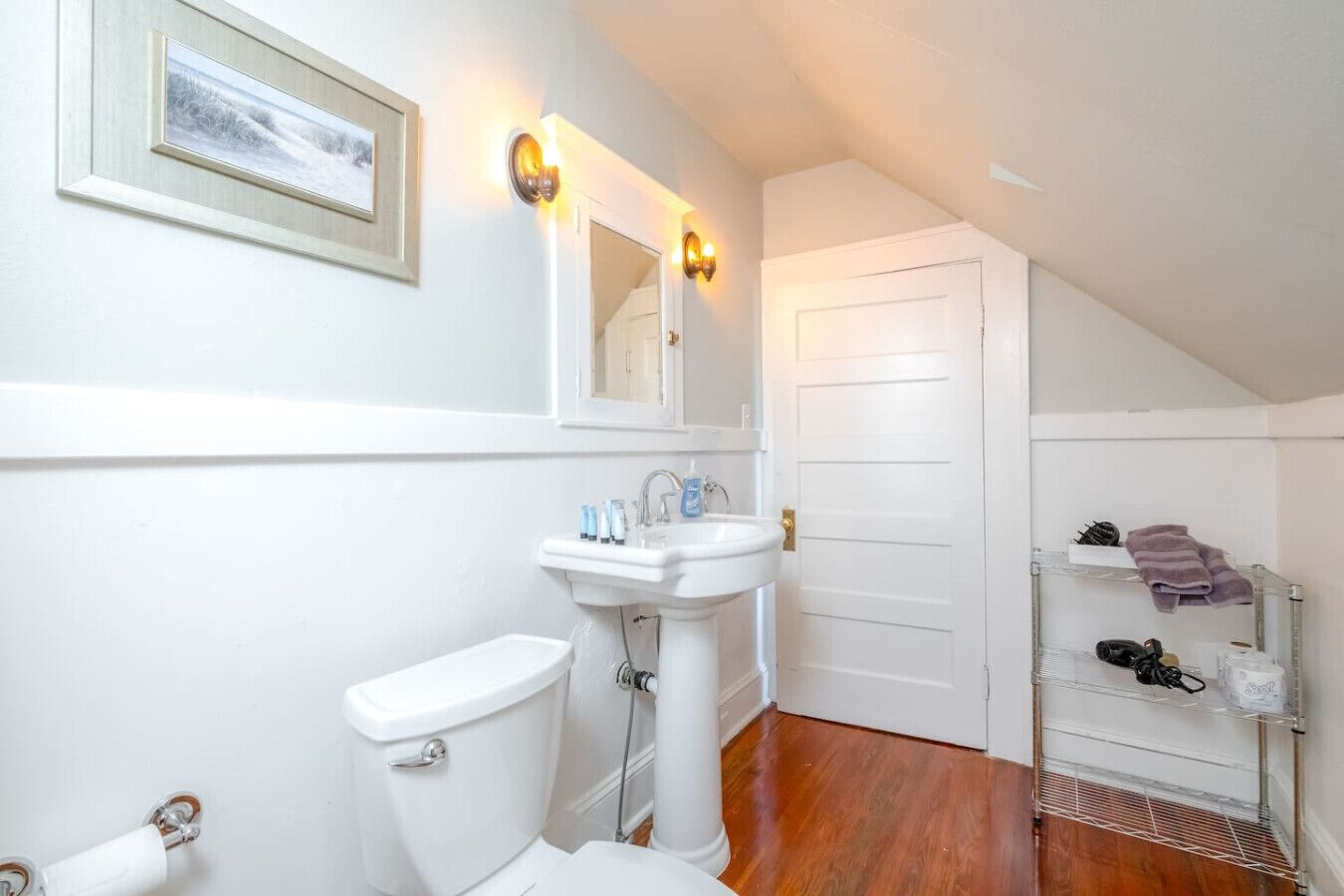A bathroom with a toilet, sink, and a mirror. There is a shelf with towels and toiletries.