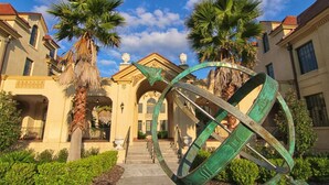 Fachada de hotel con una gran escultura verde, palmeras y arquitectura clásica.
