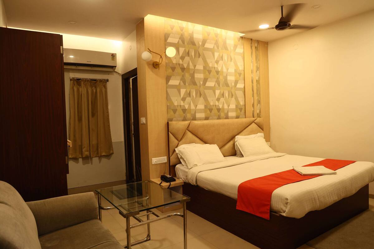 A hotel room with a bed, a glass table, a sofa, a ceiling fan, and a patterned wall.