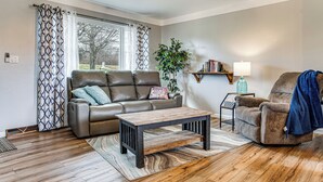 Een woonkamer met een leren bank, een houten salontafel, een fauteuil, een potplant en een boekenkast.
