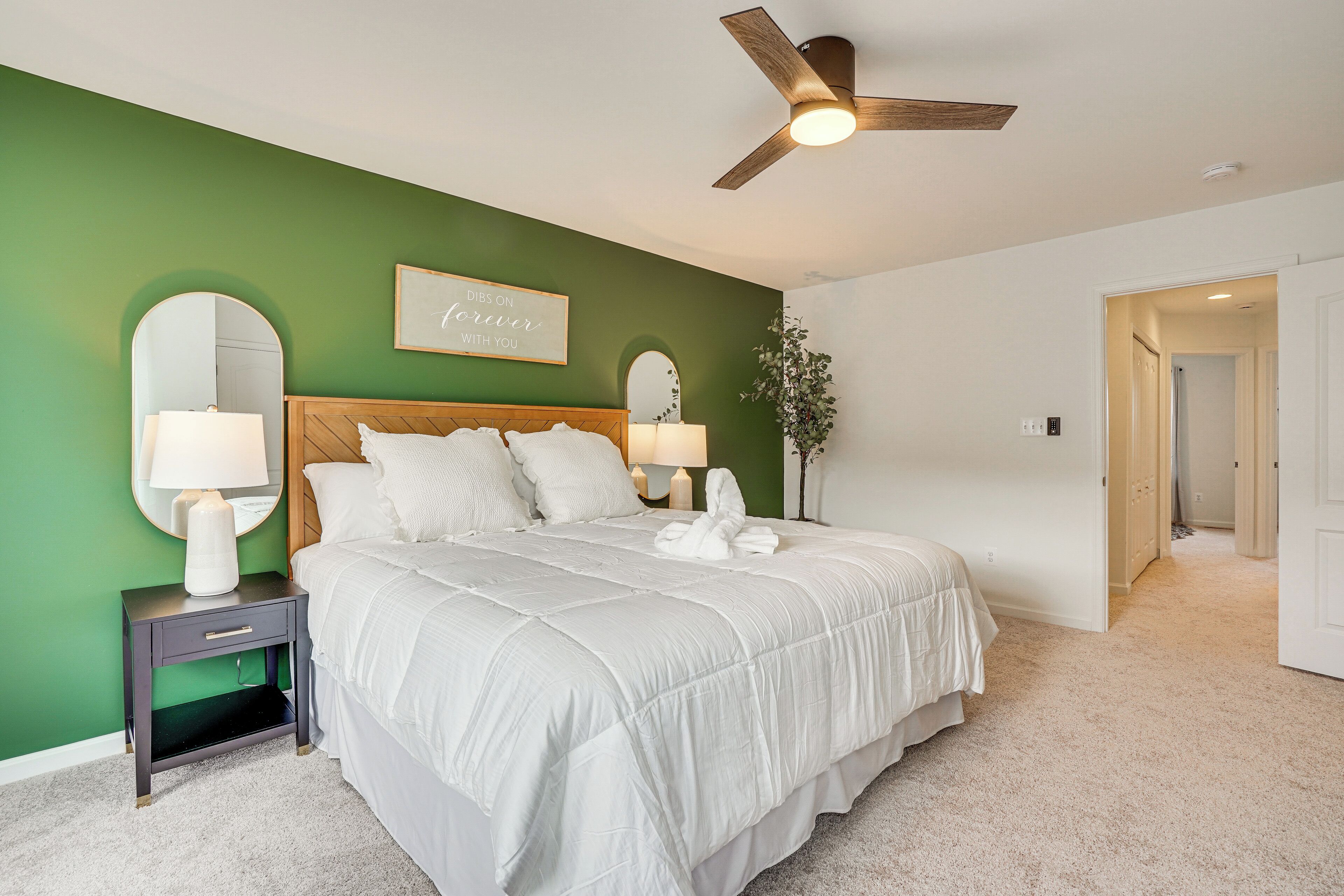 A bedroom with a large bed, two bedside tables, a ceiling fan, and a green accent wall.