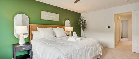A bedroom with a large bed, two bedside tables, a ceiling fan, and a green accent wall.