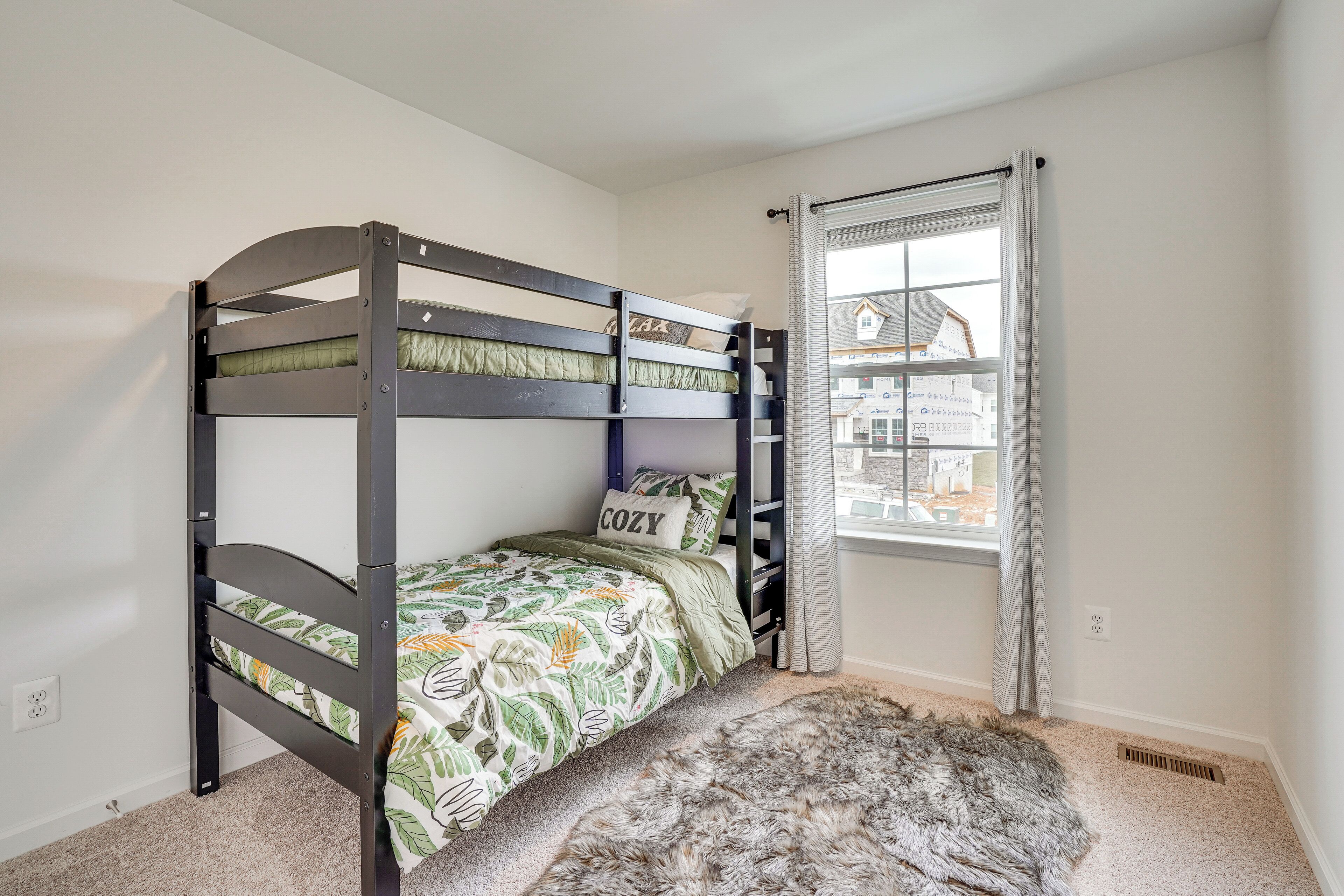 A bunk bed with a leaf-patterned bedspread, a fluffy rug, and a window with curtains.