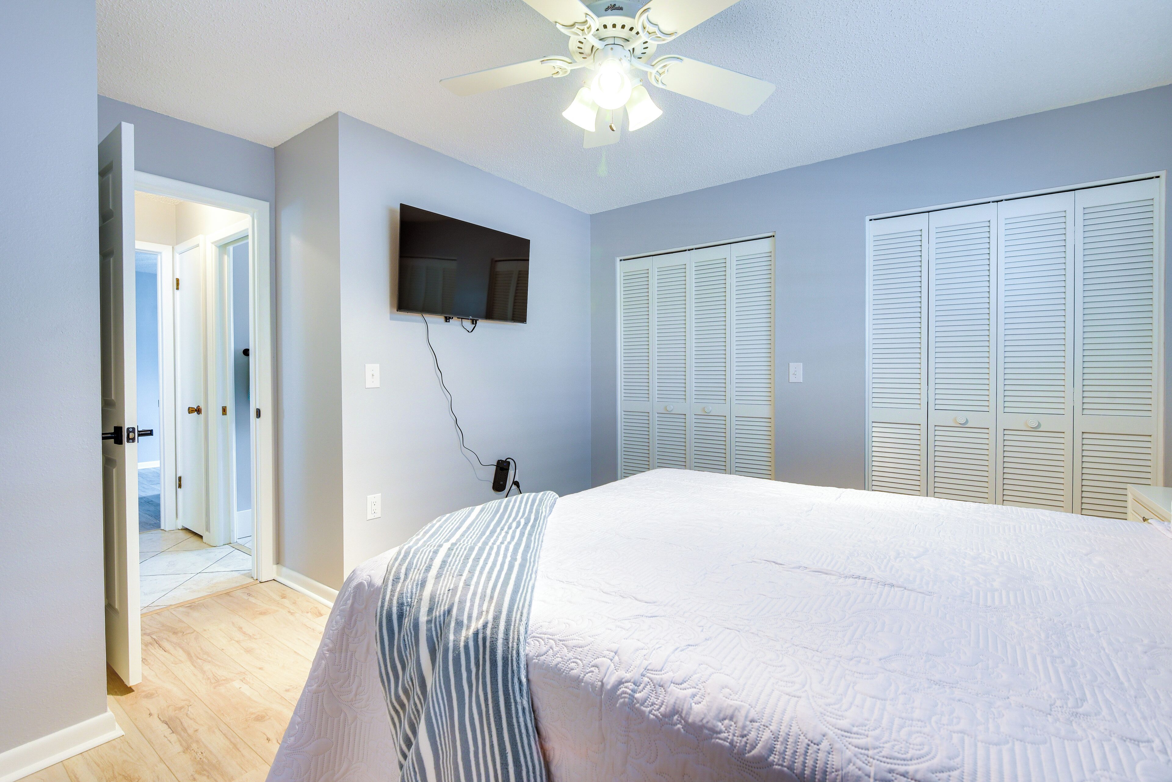 A bedroom with a bed, a ceiling fan, a TV, and a closet.