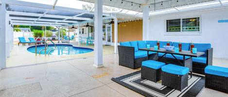 A covered outdoor area with a pool, seating, and a ceiling fan.