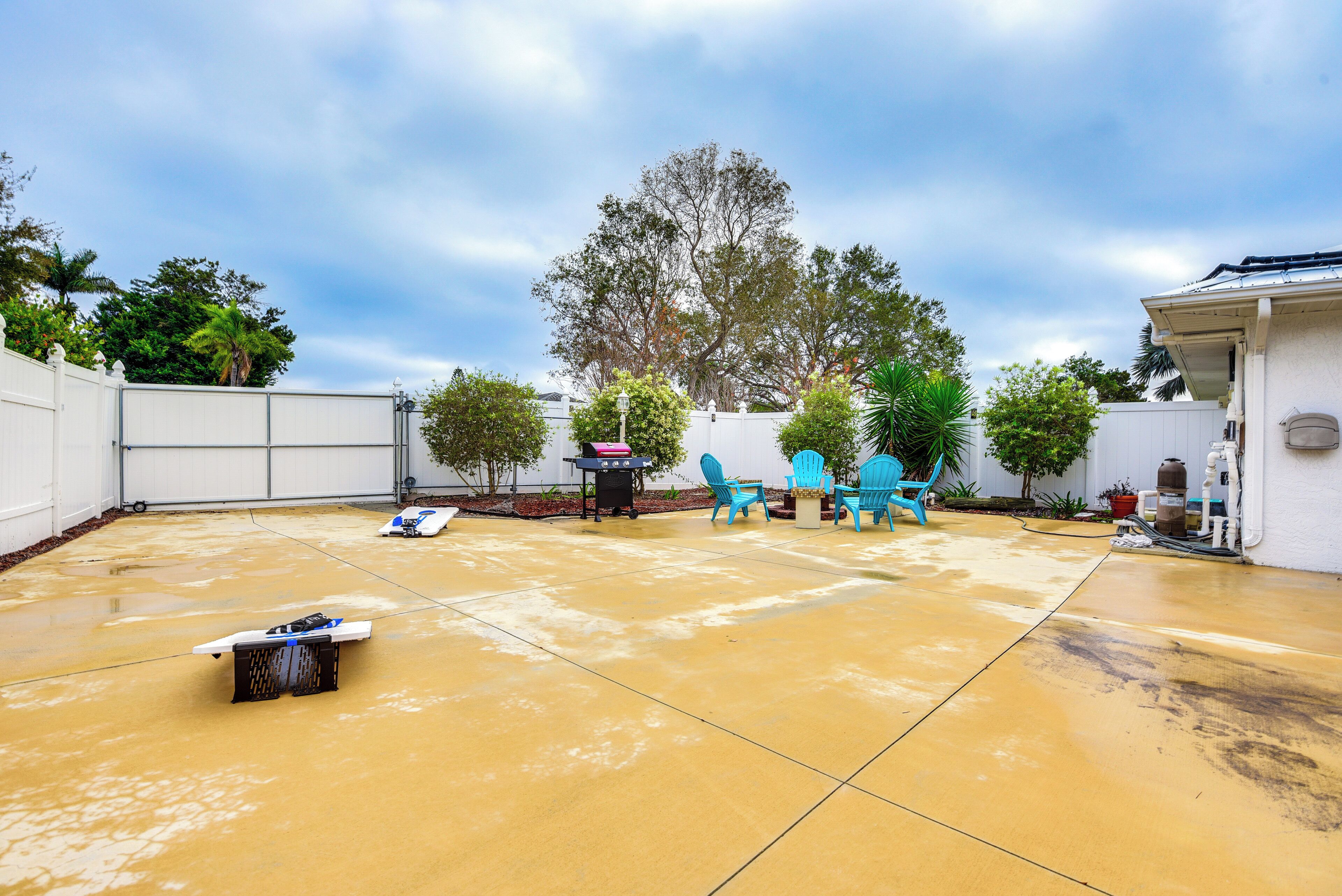 Une vaste terrasse dotée d’un sol en béton, entourée d’une clôture blanche, et agrémentée de chaises bleues et d’un barbecue.