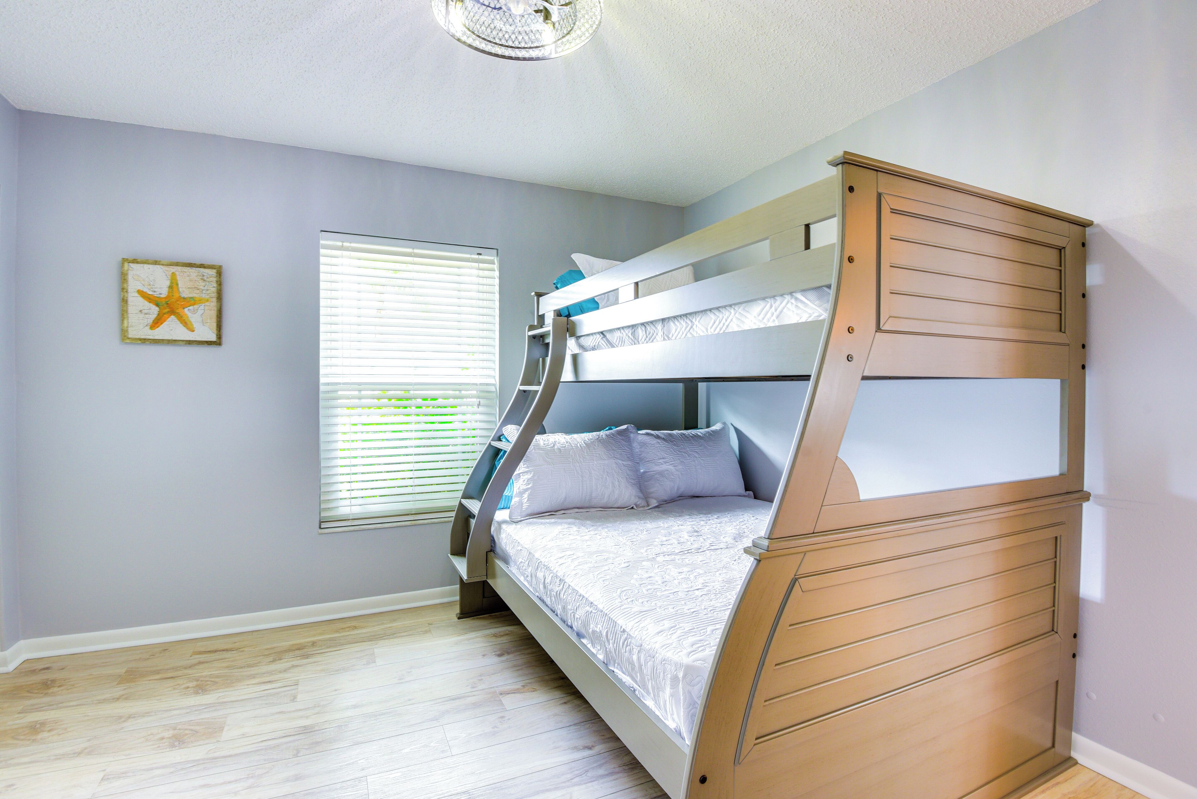 A bunk bed room with a starfish decoration, a window with blinds, and a wooden dresser.