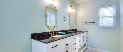 A bathroom with a double sink vanity, two wall-mounted mirrors, and a window with blinds.