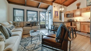 A spacious living room with a sofa, coffee table, and a leather chair. There is a kitchen area with wooden cabinets and a microwave. - Chic Greek Peak Ski Resort Townhome w/ Balconies! (Cortland)
